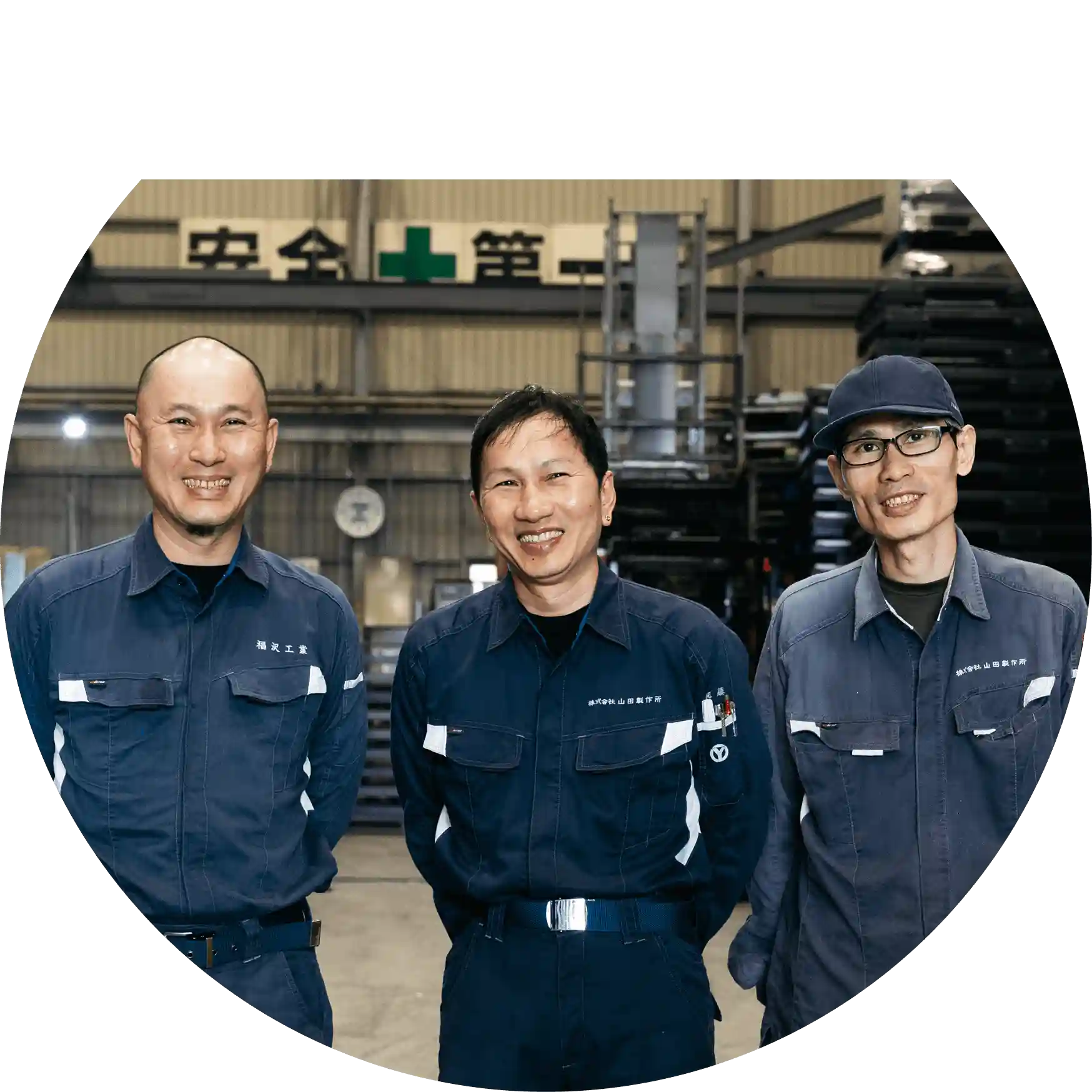 工場内で作業着を着た男性社員3人が笑顔で並んで写っている写真