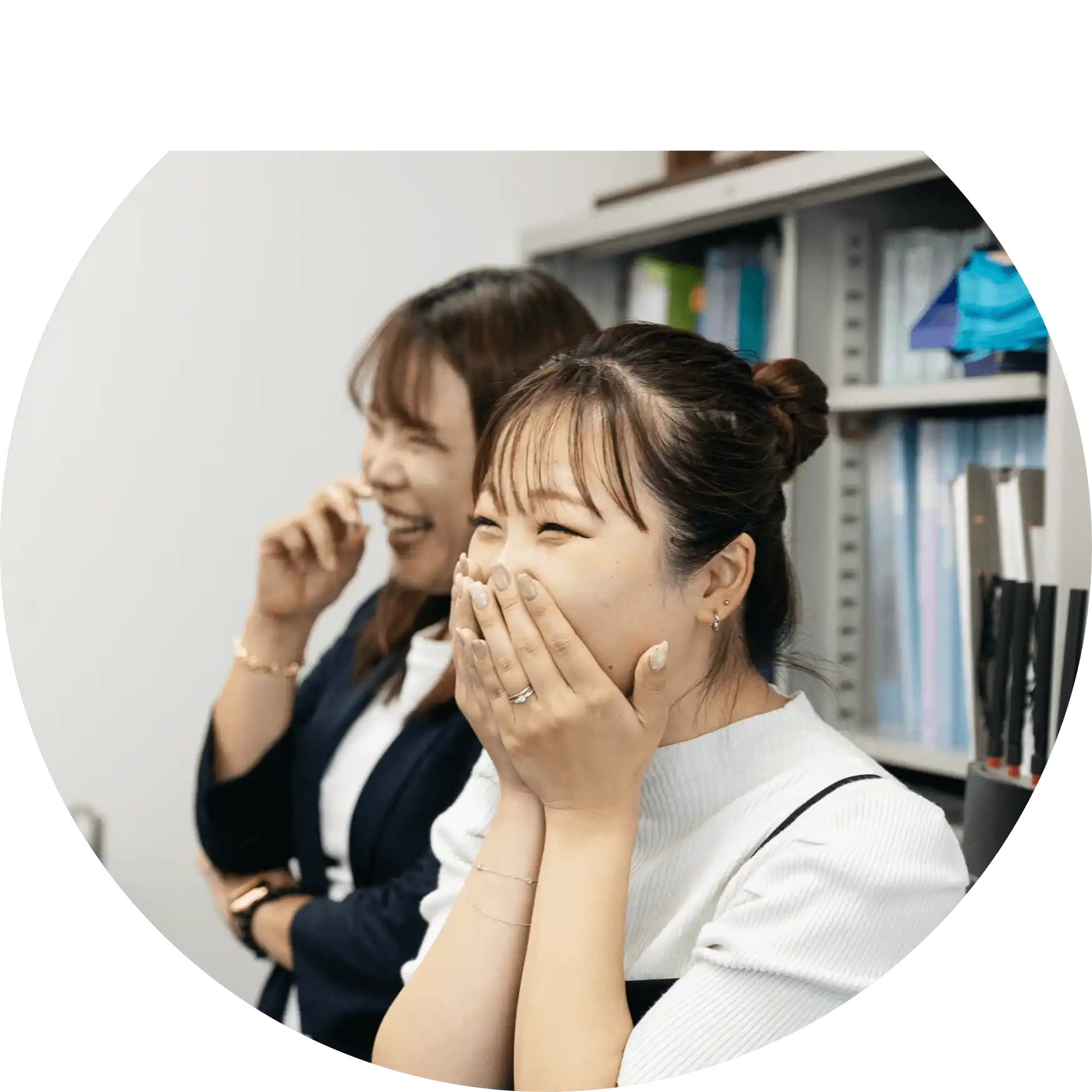 オフィス内で会話をして笑っている女性社員2人の写真