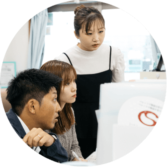 オフィス内でパソコン画面を見ながら会話をしている人物の写真